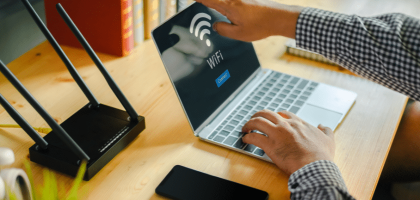 uma pessoa mexendo no notebook e ao lado um roteador de internet