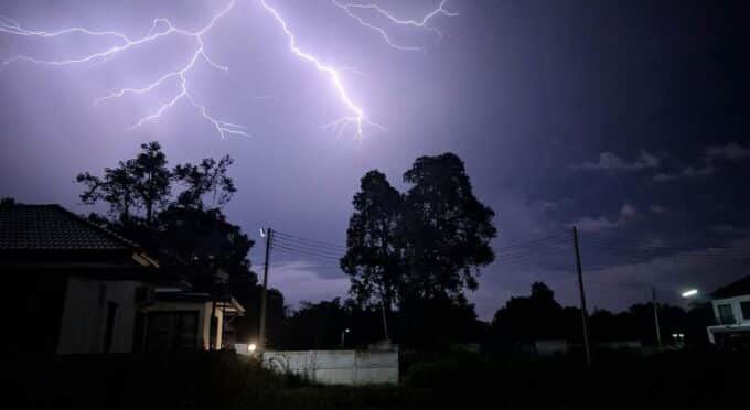 imagem de um bairro no escuro e um raio roxeado caindo sob uma árvore 