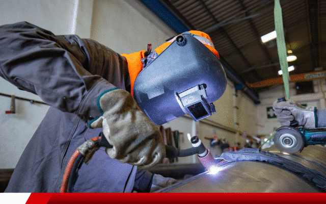 Trabalhador soldando metal com máscara de proteção.