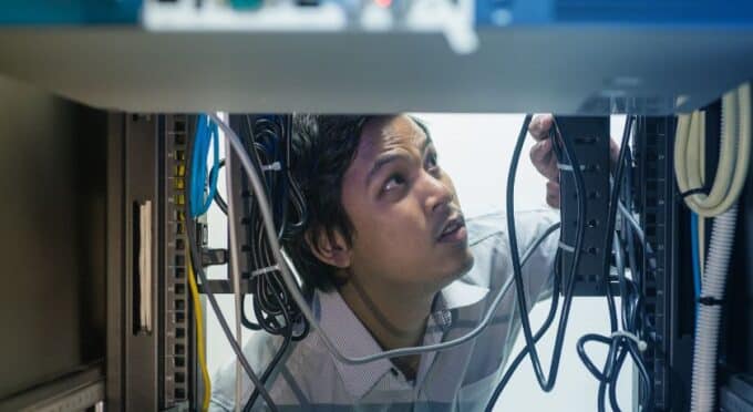 um técnico ou engenheiro olhando para cima e trabalhando em um rack de servidores.