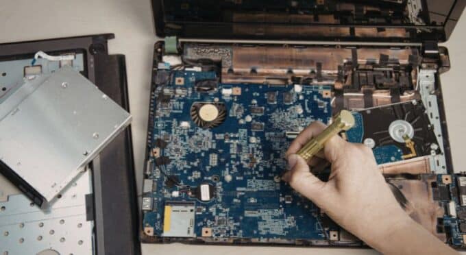 Especialista utilizando chave de fenda de precisão para manutenção interna em placa-mãe de notebook em laboratório