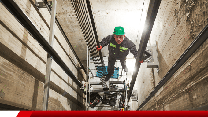 Técnico realizando manutenção em poço de elevador.
