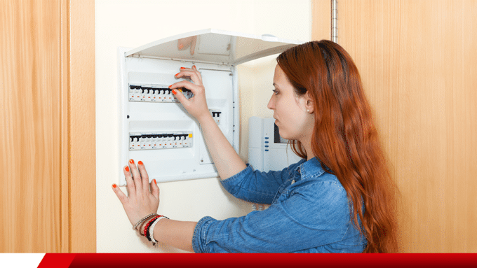 Mulher acionando disjuntor em quadro elétrico residencial.